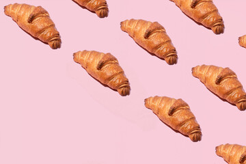 Fresh croissants, creative pattern against pastel pink background. Traditional French breakfast. 