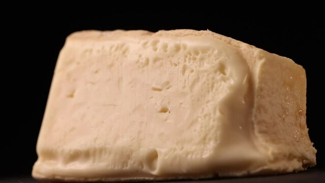 Piece of Italian, semi-soft aged Taleggio cheese rotating on cheese board, with close up detail of the texture and rind.