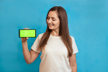 Portrait of a young girl with a phone with a green screen in her hand, on a blue background, chroma key