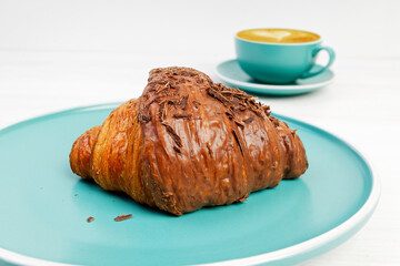 Closeup croissant with chocolate and cup of coffee cappuccino on white wooden table. Shallow focus.