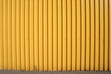 Corrugated empty yellow colored high fence made from steel sheet front view on urban street.