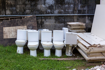 Old white discarded toilet bowls .Old toilet bowls with barrels left on the grass filed.