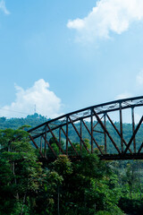 an old iron bridge in a village, with a view of a green forest