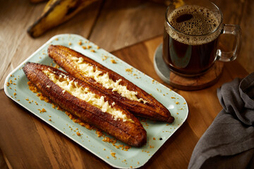 Ecuadorian maduro con queso consists of baked ripe plantains stuffed with cheese. It’s on a wooden background.  © David