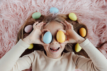 happy caucasian toddler girl eight years old at home in living room with colored easter eggs. Stay home during Coronavirus covid-19 pandemic