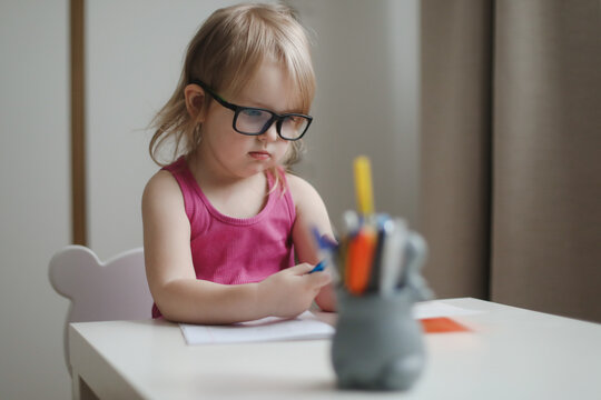 small funny girl in eyeglasses writing and drawing at the table