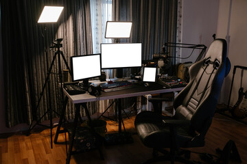 Streamer desk, workspace of a young person broadcasting on online platforms. Multiple screens and external lighting are used, gaming seat and back-mounted guitars, copy space on white screens