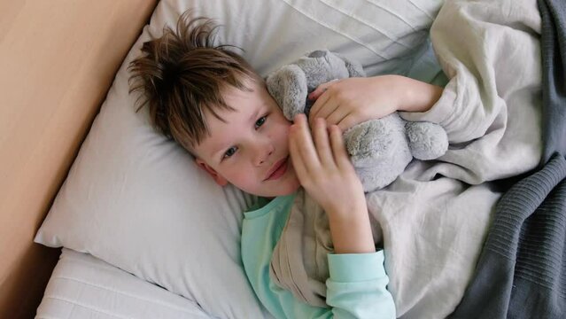 A sad boy lies on the bed with a fever and headache and rubs his head in pain. The face is twisted with pain. High quality 4k footage