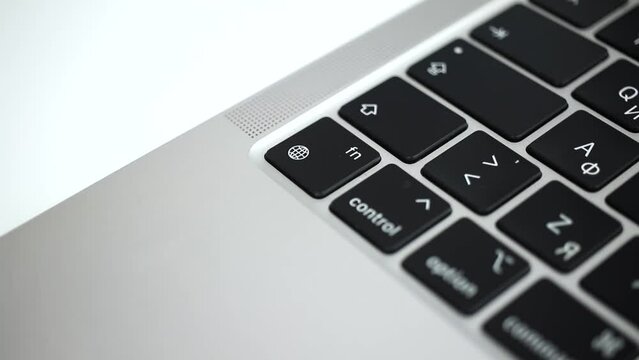 Hand pressing the globe key on modern laptop keyboard close-up slow motion 