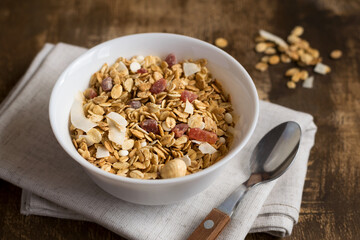 A bowl of homemade granola on a wooden table with a spoon. Granola with nuts and dried fruits for a healthy breakfast. Close-up.