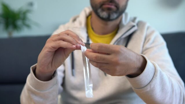Caucasian man wearing mask opening a sample of the covid-19 antigen diagnostic test device at home. A person make antigen test kit for self testing coronavirus. PCR at quarantine pandemic.