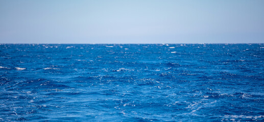 Wavy ocean water surface deep blue color, small wave with foam, blue sky background.