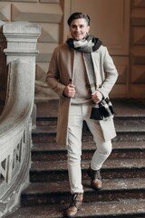  Young man wearing coat walking in the street. Young bearded guy with modern hairstyle in urban background