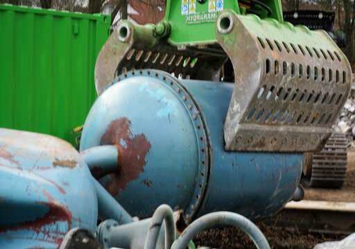 Alter blauer Filtertank aus Metall in Baggerzange aus Stahl auf Baustelle im Winter