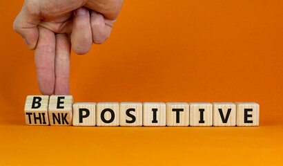 Think and be positive symbol. Businessman turns wooden cubes and changes words think positive to be positive. Beautiful orange background. Business, think and be positive concept. Copy space.