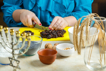 Women's hands make prunes filling for poppy-seed gomentashi cookies, traditional for the Jewish holiday Purim, on the table where there is a menorah.