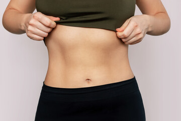 Fototapeta na wymiar Cropped shot of a young slender woman with toned stomach with abs isolated on a beige background. Result of fitness, diet, healthy lifestyle. Female belly after a lot of training. Lines and six-packs