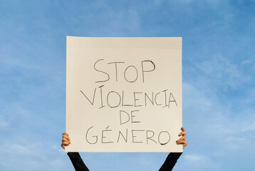manos de mujer sujetando en alto una pancarta ,protestando contra la violencia de genero, escrito en lenguaje castellano, con el cielo de fondo. - obrazy, fototapety, plakaty