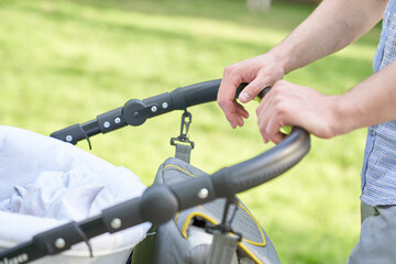 Fototapeta na wymiar Close-up of men's hands with a stroller, a young dad walking in the park with a baby in a stroller, fatherhood, dad, father's day concept. High quality photo
