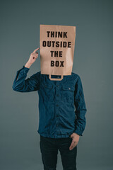 Young men has a paper bag on his head, the phrase think outside the box is standing on it,...