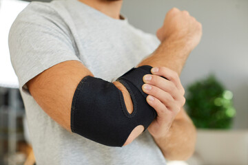 Hand injury. Close up of black elastic supportive medical bandage on elbow of man who is recovering...