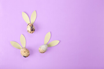 Quail eggs with rabbit ears on a lilac background. minimalistic easter background with copy space for text
