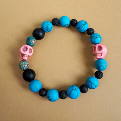 a women's bracelet made of natural stones of turquoise howlite, onyx, black lava and two pink skulls made of howlite lies on a brown background