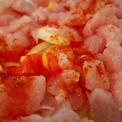 raw turkey meat cut into pieces sprinkled with red pepper, onion, potatoes before baking in the oven. side view