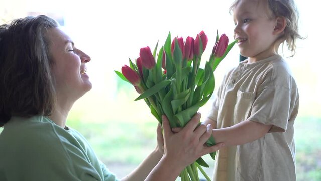 Cute blond boy gives his mother a beautiful fresh bouquet of red tulips. Mother and son, mother's day