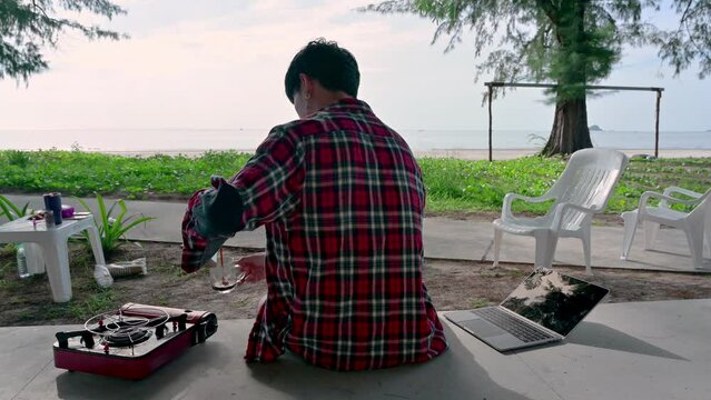 Young asian man wearing scott shirt brewing coffee and laptop at patio on vacation
