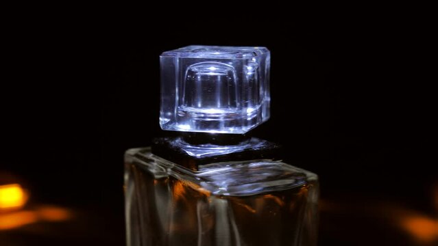 The camera pans to a close-up of a perfume bottle with a cube-shaped cap. The camera is moving. 360 degree arc tracking