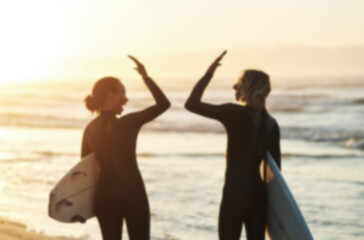 High fives and high tides. Rearview shot of a young couple joining hands for a high five while surfing at the beach.
