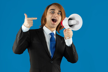 Young man using an electric megaphone. Guy with speaking-trumpet, bullhorn, blowhorn, or loudhailer. Red background. Advertising, demonstration, student protest concept