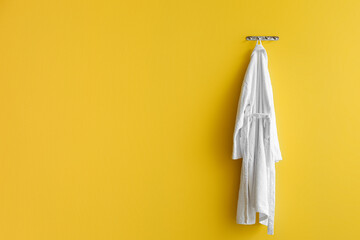 White bathrobe hanging on yellow wall - obrazy, fototapety, plakaty
