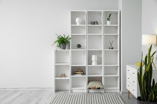 Chest of drawers with glowing lamp and big shelving unit in modern room