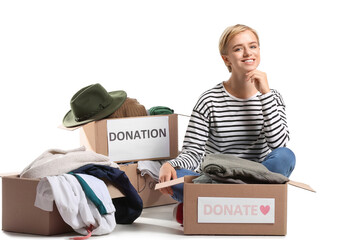 Young woman with donation clothes and boxes on white background