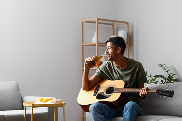 Handsome man with guitar drinking beer at home