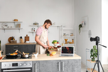 Young man cutting lettuce while following video tutorial in kitchen