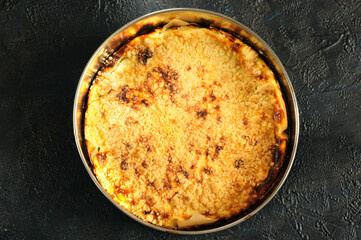 Whole golden homemade pie in a round shape on a black background. top view