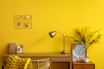 Wooden desk with golden lamp near yellow wall