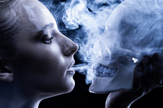 Portrait of a smoking girl with a skull in her hands on a dark background. smoking kills.