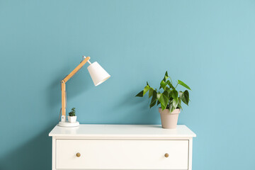 Modern lamp and houseplants on chest of drawers near blue wall