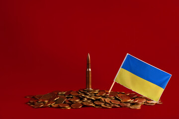The live cartridge of the Kalashnikov assault rifle with the Ukraine flag on the coins on a red...