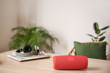 Wireless portable speaker, magazines and headphones on table in room