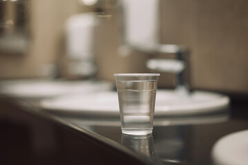 transparent plastic glass with clean water on a black table near the washbasin and water tap
