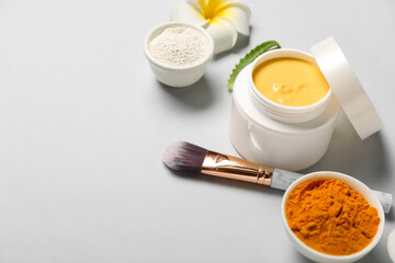 Jar with turmeric mask, powder and makeup brush on light background, closeup