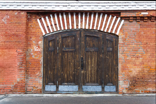 Old wooden large gate in a brick wall with an arched top