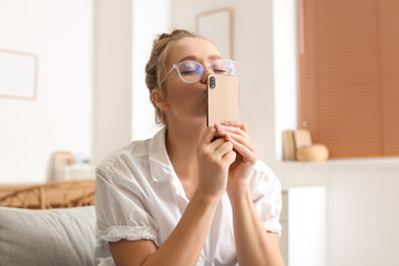 Pretty young woman kissing her mobile phone at home