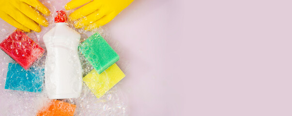 dishwashing detergent and sponges in soap suds, pink background, top view