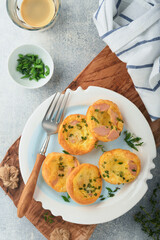 Egg muffins with green onions, bacon, cheese and tomatoes on white plate on light background. Healthy high protein and low carb breakfast, ready to eat.